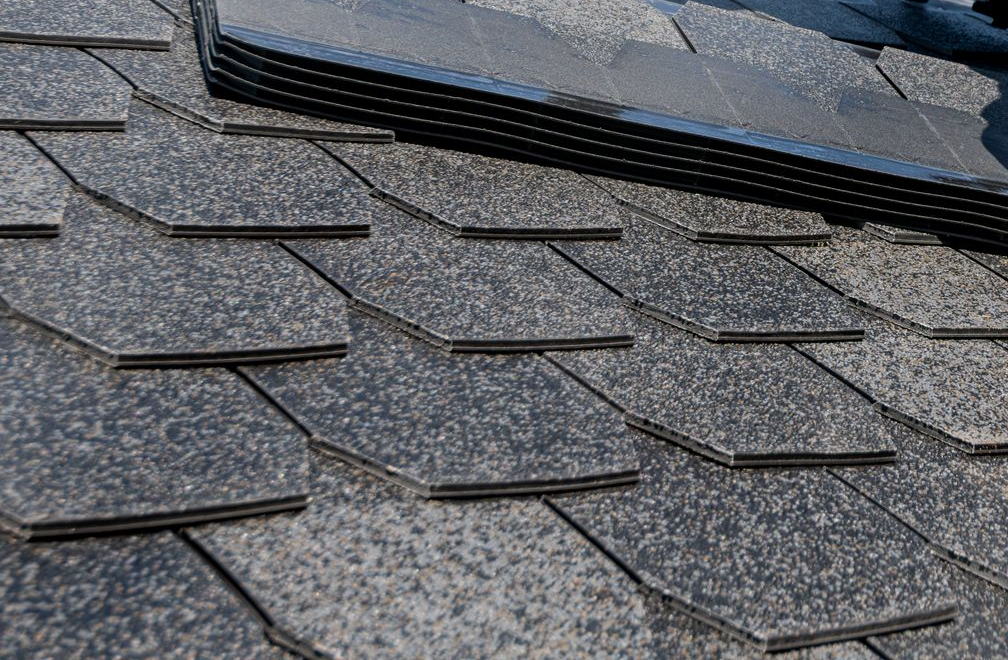 Licensed stock photograph: architectural asphalt shingles laid in staggered courses on a roof, with a stack of loose shingles waiting at the top of the run.